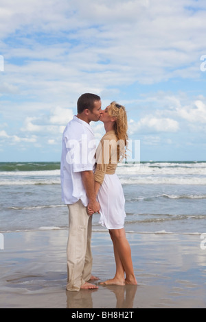 Un giovane uomo e donna tenendo le mani e baciare come una coppia romantica sulla spiaggia Foto Stock