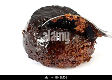 Un cucchiaio di taglio di una porzione di un piccolo di cioccolato budino di spugna con salsa Foto Stock