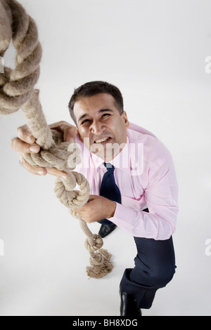 Imprenditore cerca di arrampicarsi su una corda Foto Stock