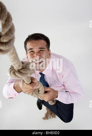 Imprenditore cerca di arrampicarsi su una corda Foto Stock