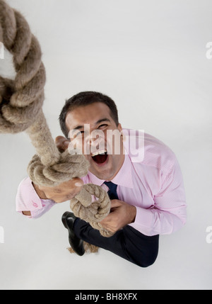 Imprenditore cerca di arrampicarsi su una corda Foto Stock