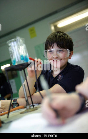 Giovane ragazzo adolescente nella scuola di scienza classe , UK, indossare occhiali di sicurezza, guardando un esperimento Foto Stock
