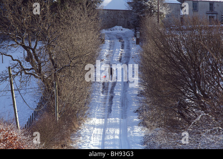 Uomo che sgombrano la neve con una pala da una lunga strada collinare di campagna in inverno, Scozia, Regno Unito Foto Stock