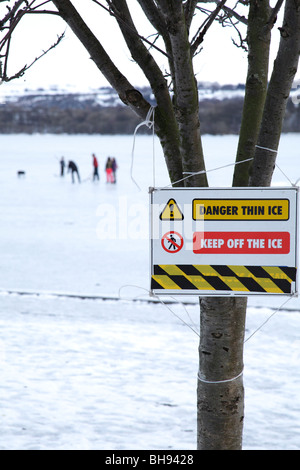 Il cartello di avvertimento di ghiaccio sottile accanto ad un Loch di Sapple del Castello congelato con la gente in inverno, il Parco Regionale di Clyde Muirshiel, Lochwinnoch, Renfrewshire, Scozia, Regno Unito Foto Stock