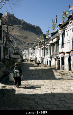 Donna tibetana nel tradizionale quartiere vecchio di gyantse con il dzong su di una collina nella distanza Foto Stock