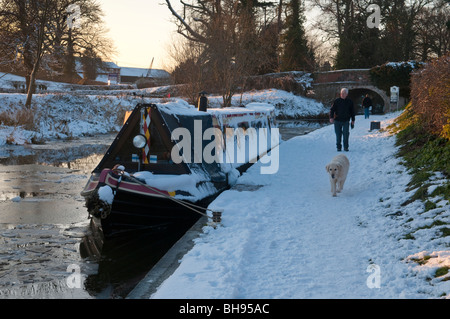 Uomo che cammina cane sulla strada alzaia accanto congelati LLangollen Canal in inverno a Ellesmere, Shropshire Foto Stock