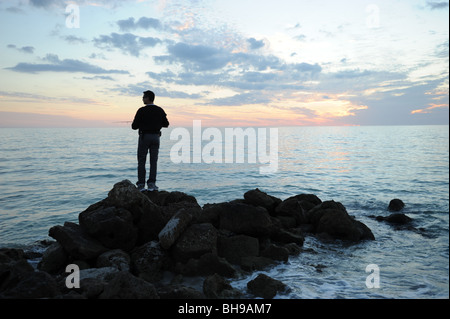 Pescatore solitario si fermò sulle rocce contro un tramonto spettacolare sulla spiaggia di Naples, Florida USA Foto Stock