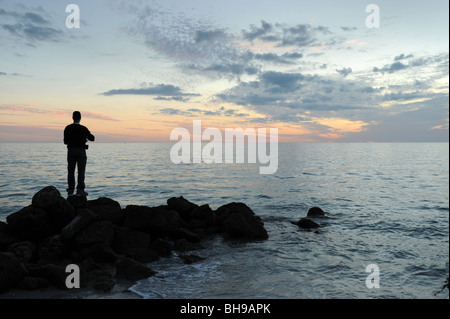 Pescatore solitario si fermò sulle rocce contro un tramonto spettacolare sulla spiaggia di Naples, Florida USA Foto Stock