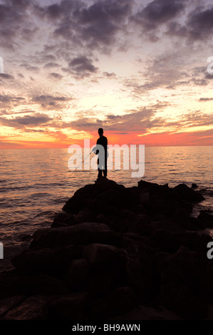 Pescatore solitario si fermò sulle rocce contro un tramonto spettacolare sulla spiaggia di Naples, Florida USA Foto Stock