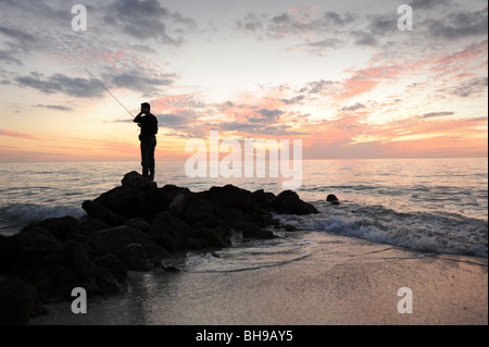 Pescatore solitario si fermò sulle rocce contro un tramonto spettacolare sulla spiaggia di Naples, Florida USA Foto Stock