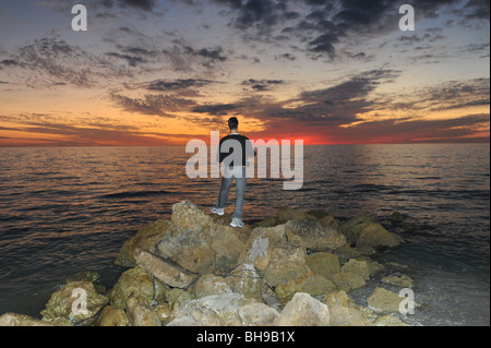 Pescatore solitario si fermò sulle rocce contro un tramonto spettacolare sulla spiaggia di Naples, Florida USA Foto Stock