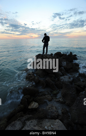 Pescatore solitario si fermò sulle rocce contro un tramonto spettacolare sulla spiaggia di Naples, Florida USA Foto Stock