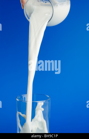 Flusso di latte che viene versato in un bicchiere su sfondo blu. Foto Stock