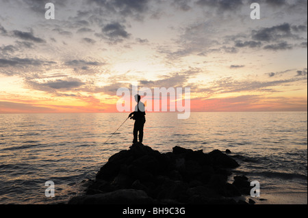 Pescatore solitario si fermò sulle rocce contro un tramonto spettacolare sulla spiaggia di Naples, Florida USA Foto Stock