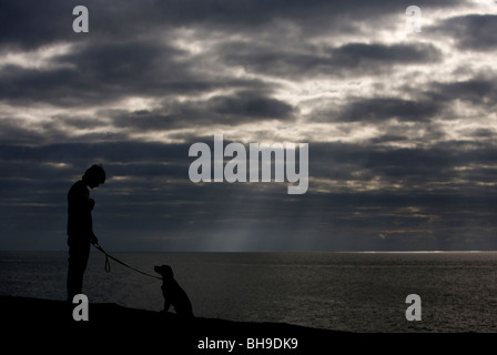 Ragazzo e cane singolo ragazzo adolescente con Labrador cucciolo Silhouette Chesil Beach, Dorset, Regno Unito Foto Stock