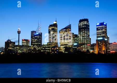 Skyline di Sydney da Mrs Macquarie's Point Sydney Australia // SYDNEY, Australia - Vista dal tramonto dello skyline di Sydney visto da Mrs. Macquarie's Point. Gli edifici iconici della città, tra cui la Sydney Tower, sono illuminati in modo luminoso contro il cielo blu intenso al crepuscolo, riflettendo dolcemente sull'acqua in primo piano. Questo punto panoramico offre una prospettiva classica del vibrante paesaggio urbano. Foto Stock