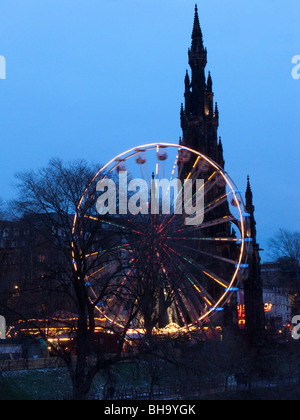 Winter Wonderland luna park con le luci della notte prese al tramonto con grande ruota contro il Monumento di Scott Edimburgo, Scozia UK Foto Stock