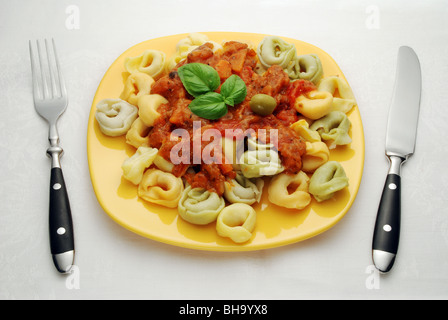 Tortellini multicolori con salsa di pomodoro sulla piastra di giallo, servendo con coltello e forchetta Foto Stock