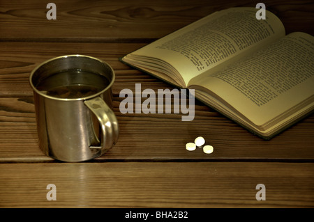 Concetto di single la vita degli anziani. Mug, pillole e prenota su una scrivania in legno. Foto Stock