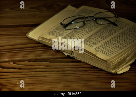Bicchieri e vecchio libro (dizionario) su una scrivania in legno. Foto Stock