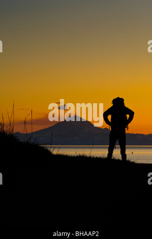 Escursionista guardando attraverso Cook Inlet pennacchio in salita da Mt. Redoubt, Penisola di Kenai, centromeridionale Alaska, molla Foto Stock