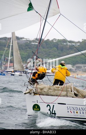 Da Rolex Sydney a Hobart Yacht Race Sydney Australia | SYDNEY, Australia - l'equipaggio a bordo dello yacht Sundance esegue un'asta spinnaker pochi istanti dopo l'inizio della Rolex Sydney a Hobart Yacht Race nel porto di Sydney. Il loro pesante equipaggiamento offshore segnala la preparazione per l'estenuante percorso di 628 miglia nautiche verso la Tasmania. La gara del giorno di Santo Stefano conduce i concorrenti attraverso lo stretto di Bass, notoriamente volatile, dove acque poco profonde e forti venti spesso generano condizioni di mare difficili. Foto Stock