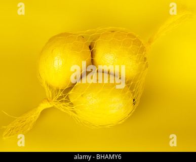 Tre gialli di limoni in una stringa-bag su uno sfondo giallo. Foto Stock