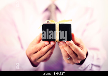 Business man in tuta che offre piccoli confezione regalo dritto per la fotocamera Foto Stock