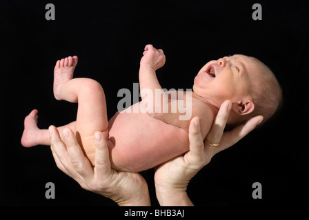 Neonato tenuto nella mani dei Padri isolato sul nero, di età compresa tra i 13 giorni Foto Stock