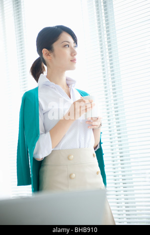 Giappone, nella prefettura di Osaka, imprenditrice con tazza di caffè, guardando lontano Foto Stock