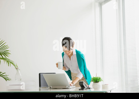 Giappone, nella prefettura di Osaka, imprenditrice con tazza da caffè utilizzando laptop Foto Stock