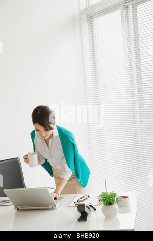 Giappone, nella prefettura di Osaka, imprenditrice con tazza da caffè utilizzando laptop Foto Stock