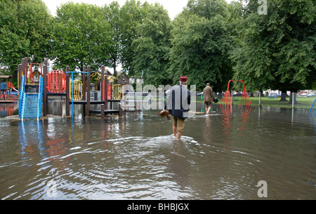 2 uomini musulmani camminare attraverso allagato il parco giochi nel parco con pantaloni arrotolata. Foto Stock