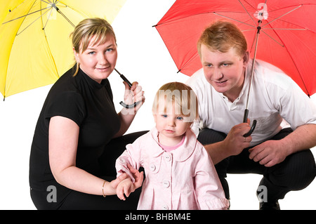 Giovane famiglia russa caucasici seduto sotto gli ombrelloni di colore in studio. Tagliare Foto Stock