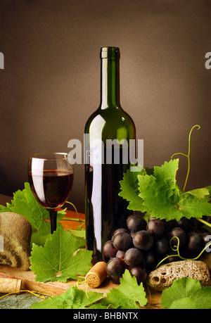 Natura morta con un bicchiere di vino rosso bottiglia, vetro, uve fresche e foglie di vite su sfondo scuro Foto Stock