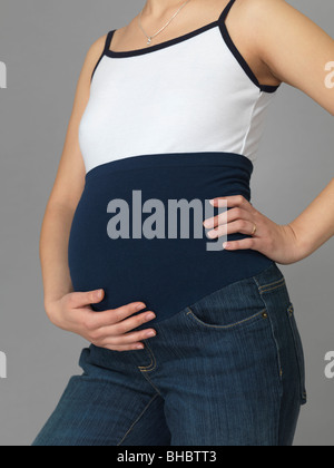 Incinta giovane donna indossa jeans di maternità di un tratto di nastro intorno al suo ventre Foto Stock