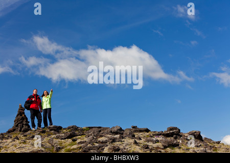 Una giovane coppia escursioni nelle montagne pietrose in piedi accanto a una pila di pietra tor o signpost puntando alla distanza. Foto Stock