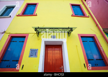 Una luminosa casa gialla con il rosso e il blu windows, Burano, Venezia Foto Stock