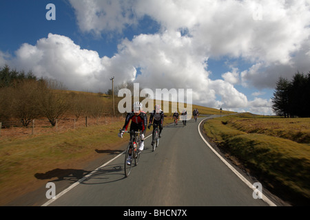 Gruppetto di ciclisti in corsa giù per una strada chiusa attraverso la campagna Foto Stock