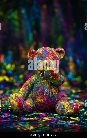 Orsacchiotto di peluche seduto su un panno nero coperto di polvere colorata. Still Life Foto Stock