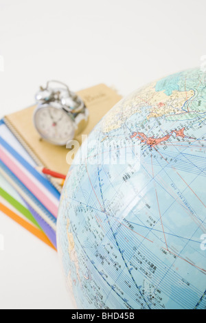 Pila di notebook con matite e sveglia con globo in primo piano Foto Stock