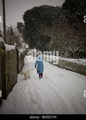 Una donna cammina il suo cane lungo una strada di campagna nella neve Foto Stock