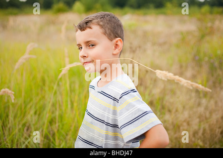 Carino kid masticare una cannuccia di erba gialla, come l'agricoltore egli è Foto Stock