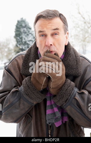 Senior uomo in piedi fuori nel paesaggio innevato Mani di riscaldamento Foto Stock