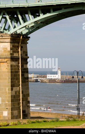 Spiaggia di South Bay e faro del porto incorniciati da uno dei moli di pietra del ponte Spa, Scarborough. Foto Stock