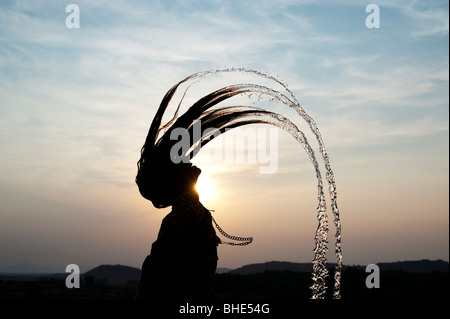 Ragazza indiano gettando i suoi capelli bagnati indietro causando uno spruzzo di acqua silhouette. India Foto Stock