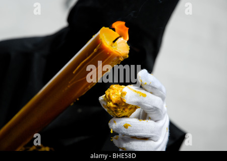 Il penitente della settimana Santa porta una grande candela processionale durante la celebrazione pasquale a Malaga, Spagna. Foto Stock