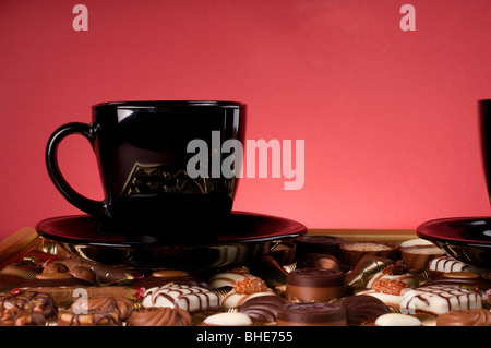 Black Coffee Cup oltre i dolci al cioccolato nella casella d'oro su sfondo rosso. Foto Stock