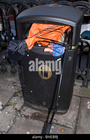 Rotto abbandonato arancione e nero ombrello oggetto di dumping in un bidone della spazzatura in Bath Somerset REGNO UNITO Foto Stock