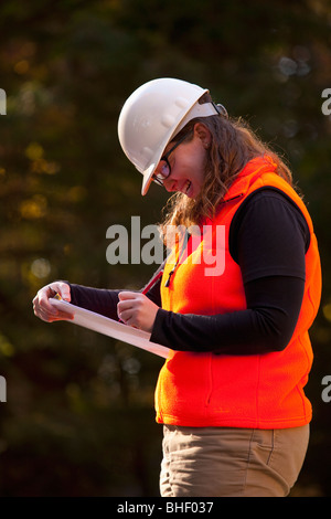 Ingegnere femmina la scrittura su un blocco appunti in corrispondenza di un sito in costruzione Foto Stock